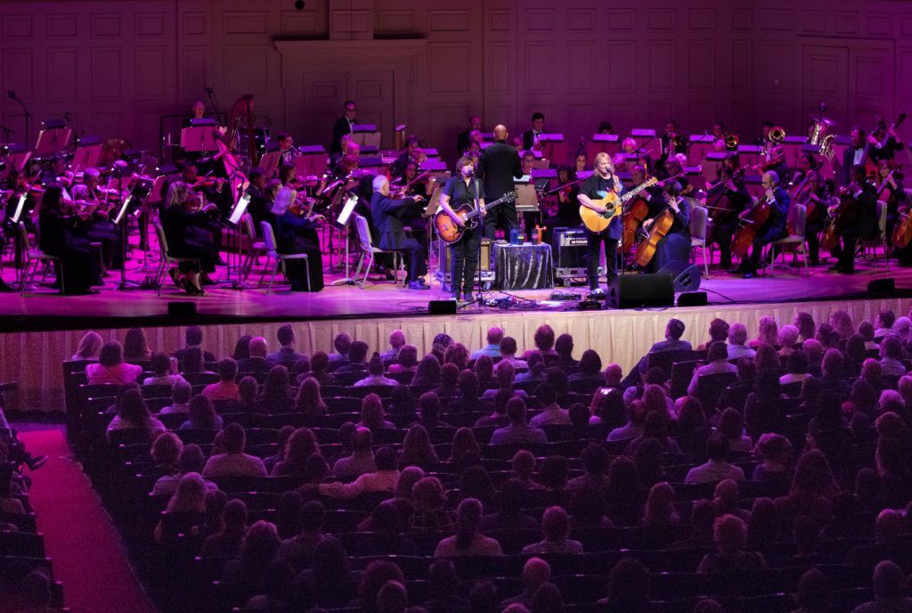 A man is playing a guitar on a stage in front of an orchestra.