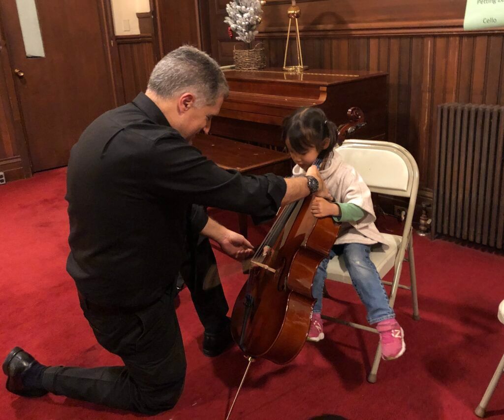 A man is helping a little girl play a cello.
