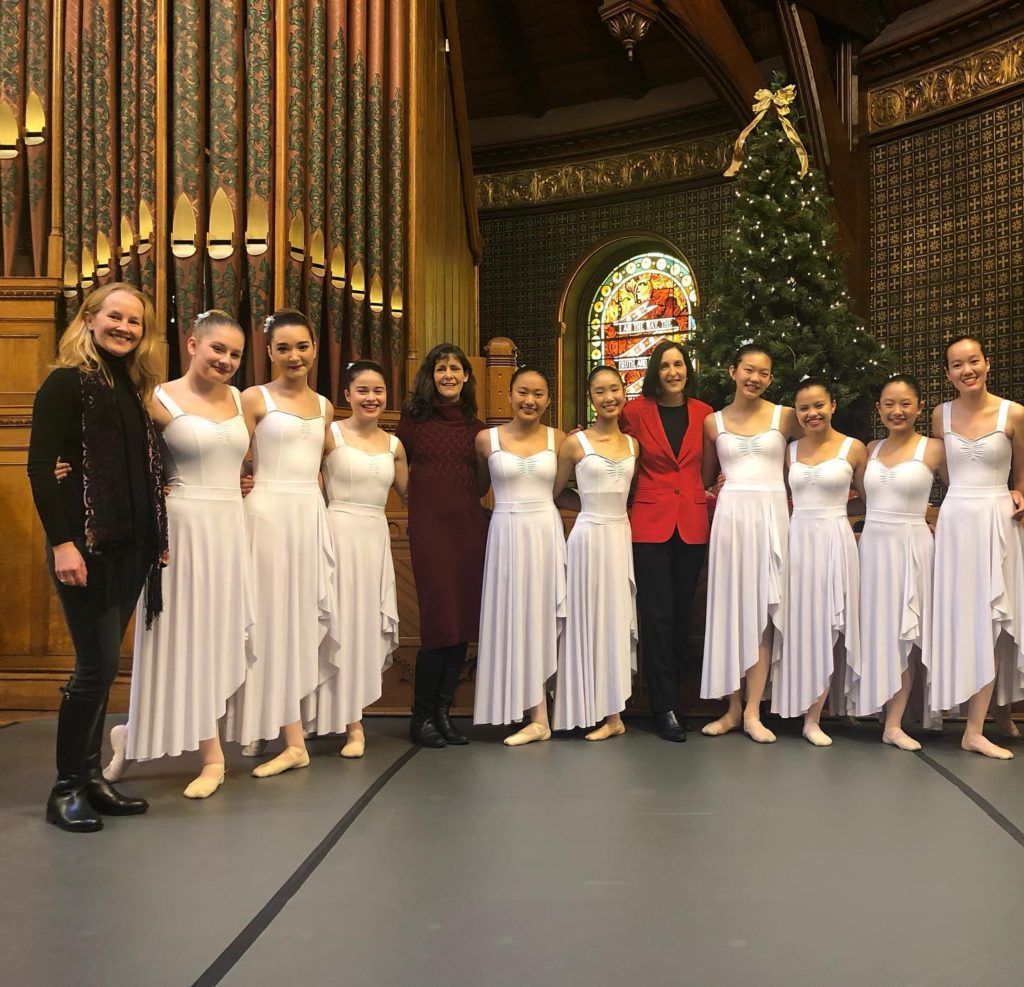 A group of women in white dresses are posing for a picture in front of a christmas tree.