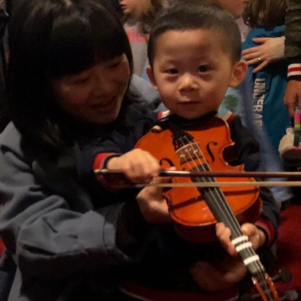 A woman is holding a child who is playing a violin