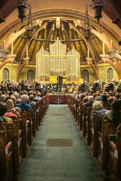 A large group of people are sitting in a church watching a concert.