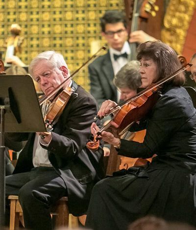 A man and a woman are playing violins in an orchestra