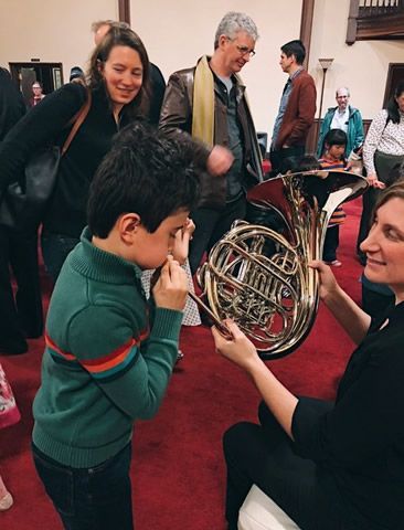 A woman is holding a french horn while a boy looks on