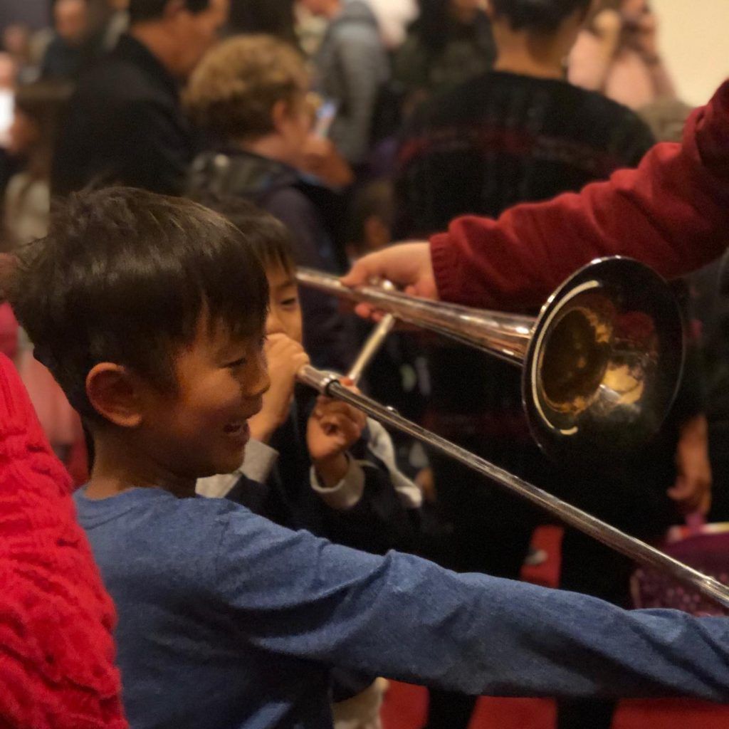 A boy in a blue shirt is playing a trombone