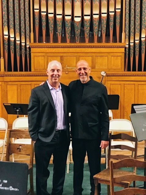 Two men are posing for a picture in front of an organ in a church.