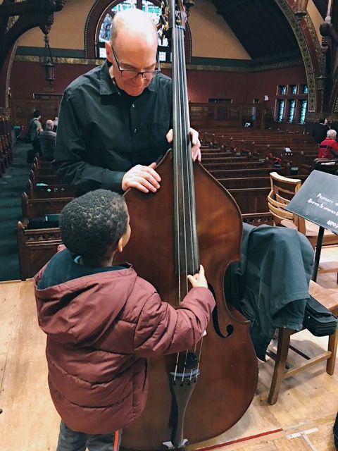 A man is teaching a young boy how to play a double bass