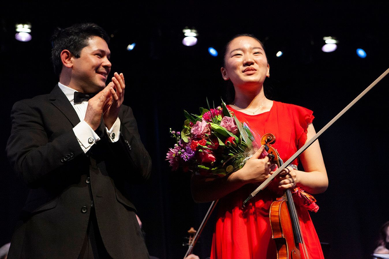 A woman in a red dress is holding a violin next to a man in a suit.