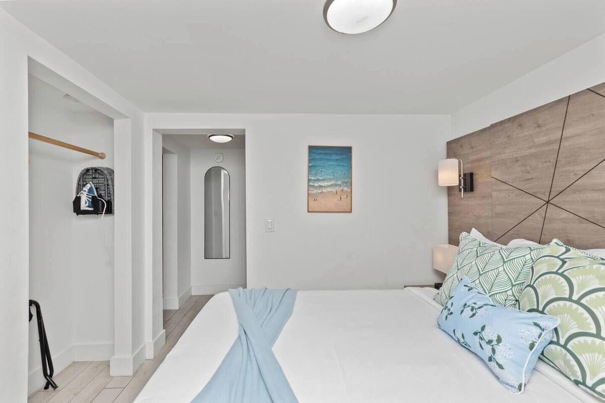 Bedroom with bed, closet, and artwork. White walls, light wood headboard, and blue accent pillows.
