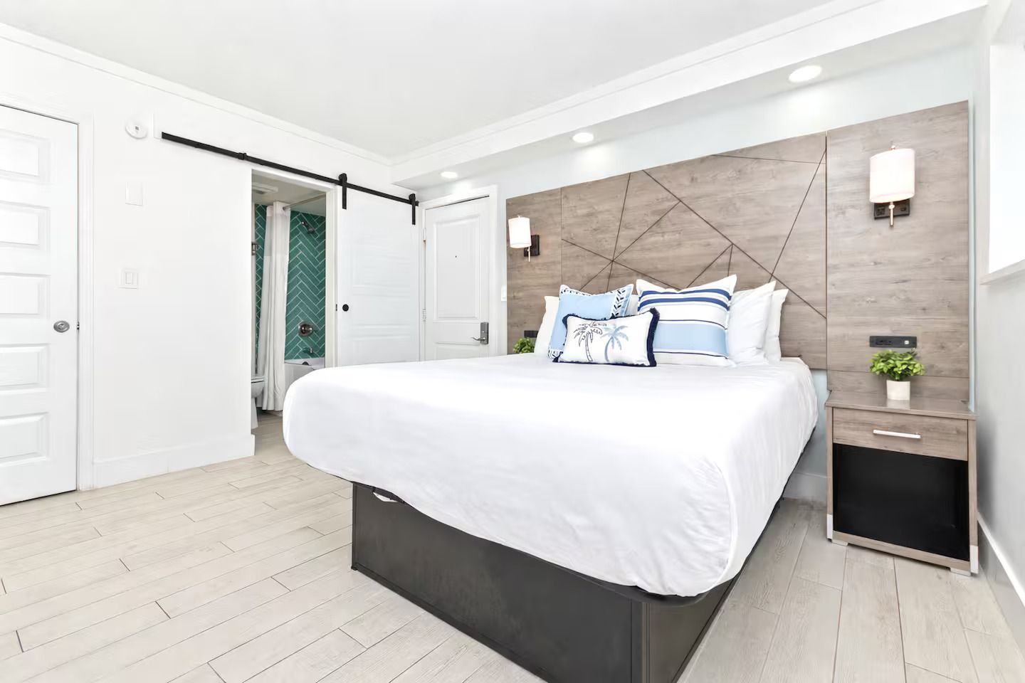 Bedroom with a bed, nightstand, and sliding door to a bathroom. Light blue and white decor.
