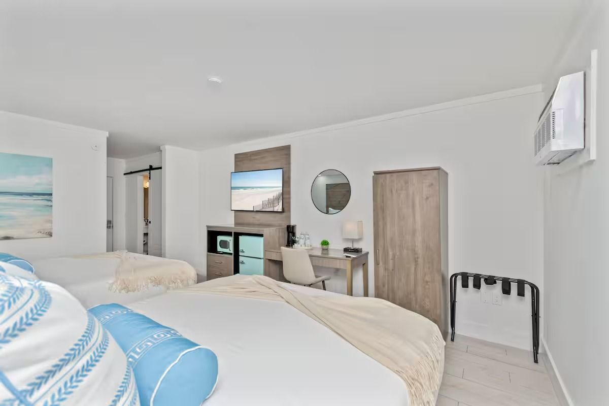 Hotel room with two beds, desk, TV, and luggage rack. White walls, blue and beige decor.