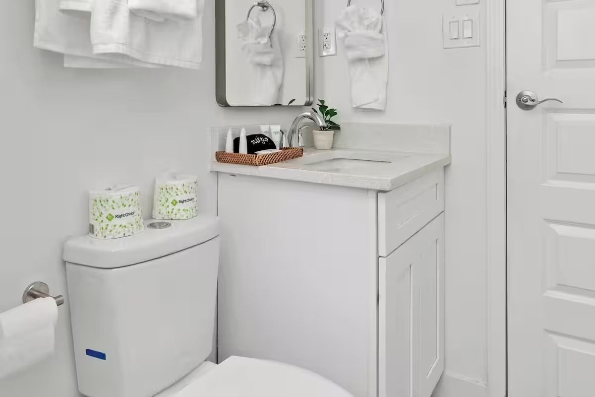 Small white bathroom with toilet, sink, mirror, and towels.