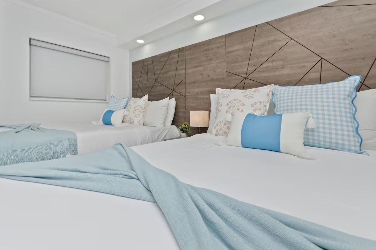 Bedroom with two queen beds, light blue accents, textured headboard, and soft lighting.