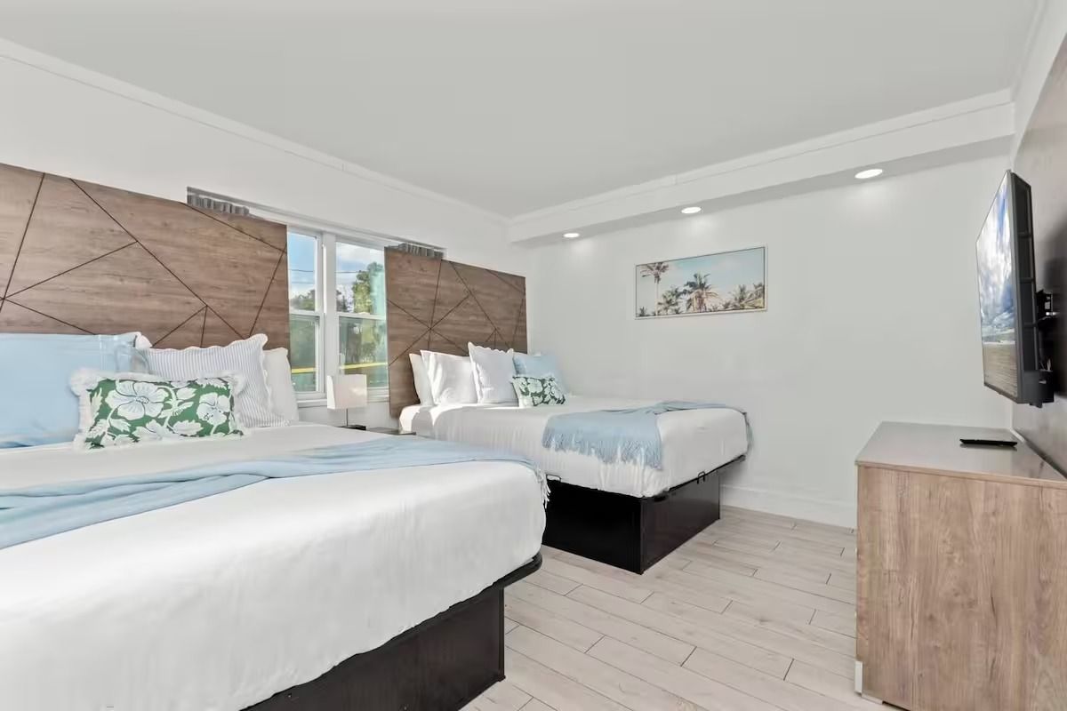 Hotel room with two beds, one large, one smaller, light blue and white bedding, wooden headboards.