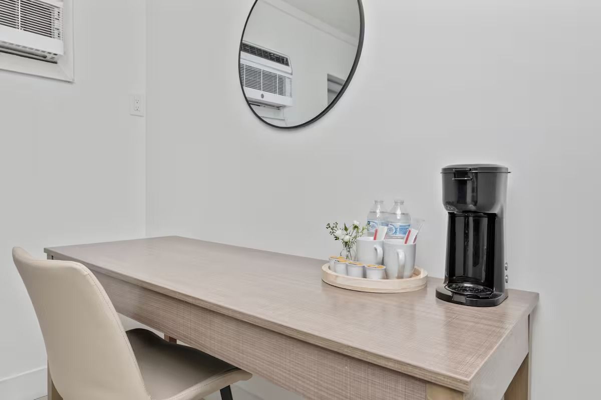 Desk with coffee maker, water bottles, and a mirror in a room.