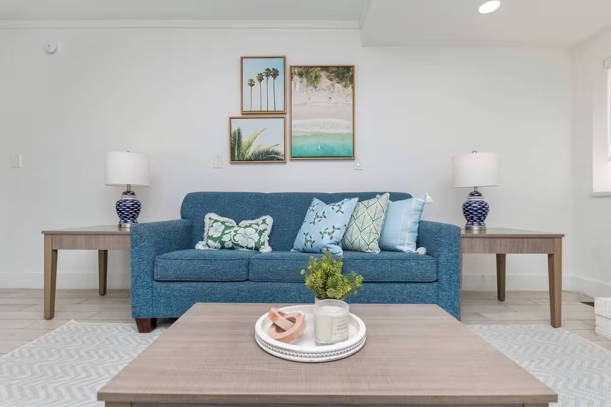 Blue couch in a white-walled living room with beach-themed art, lamps, and a coffee table.