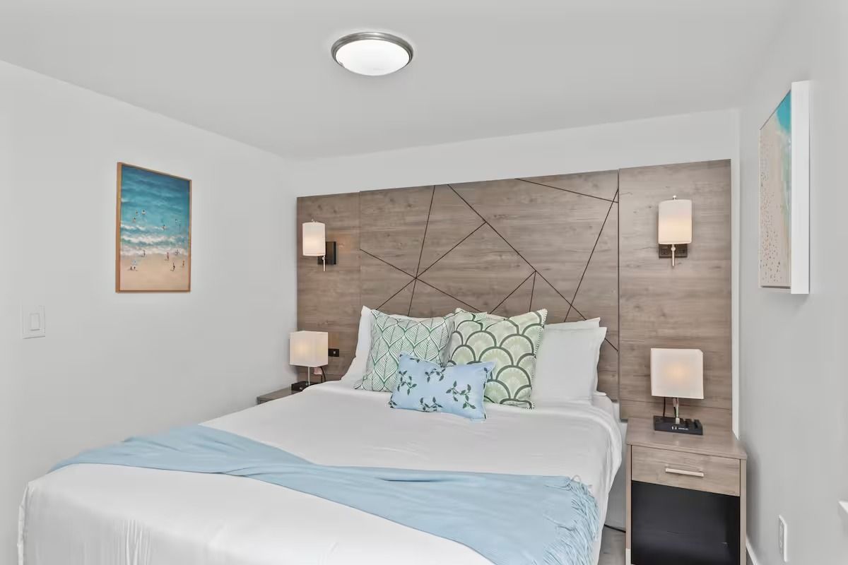 Bedroom with bed, headboard, side tables, wall art, and lamps; light blue accents.