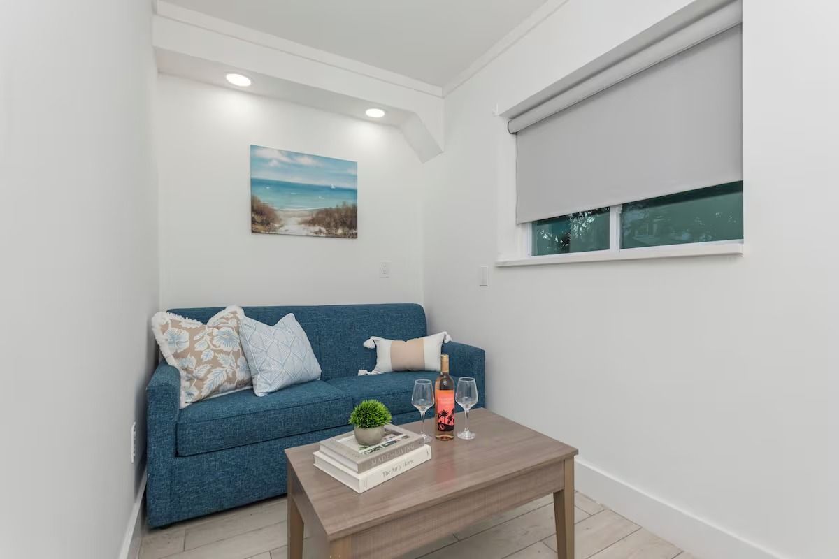 Small living area with blue sofa, small table, artwork, and window with blinds.