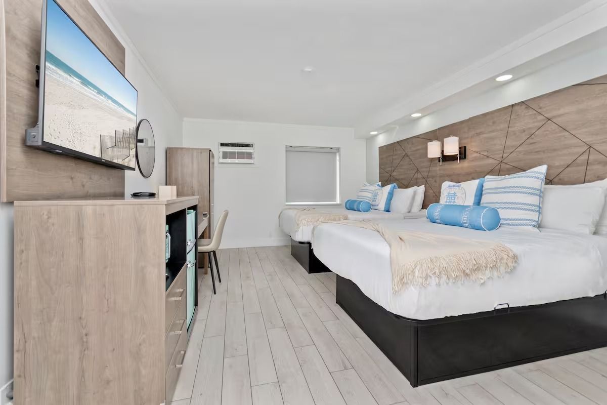 Hotel room with two beds, TV, desk, and light wood accent wall.