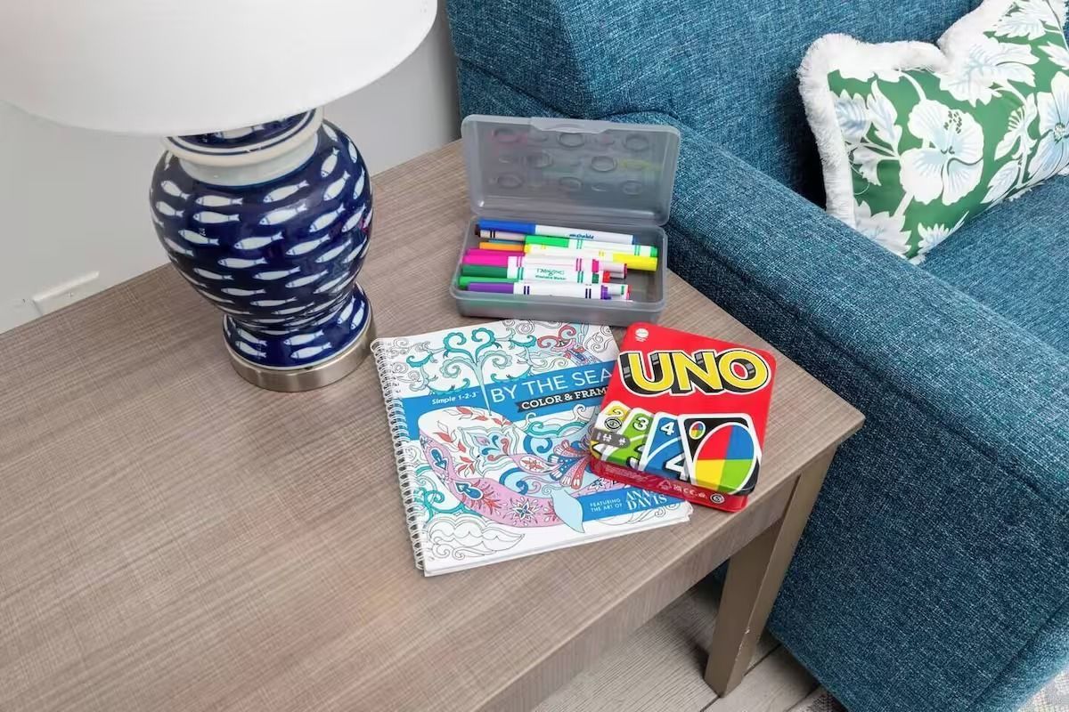 A table with a lamp, markers, coloring book, and UNO cards next to a blue couch.
