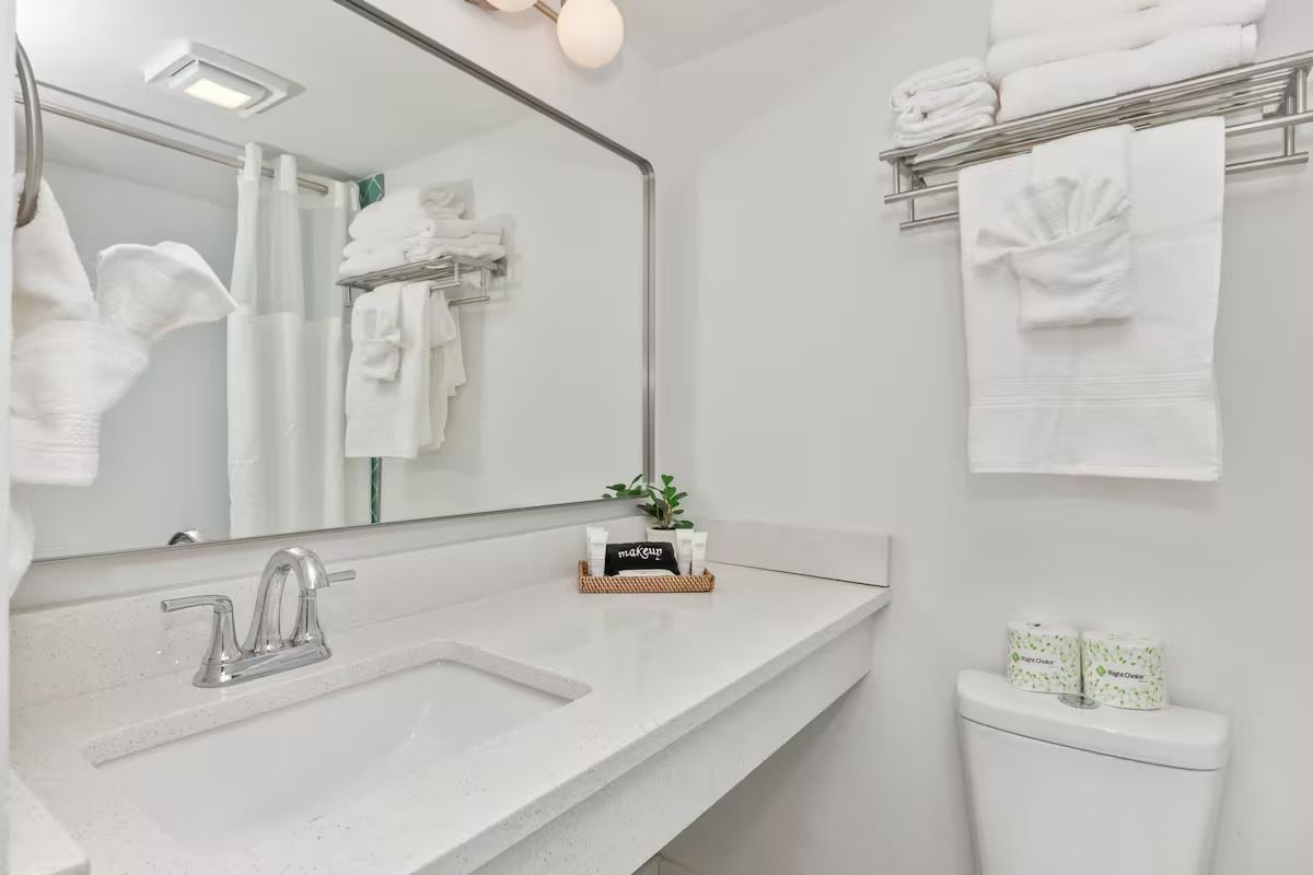 White hotel bathroom with a sink, mirror, and towels.