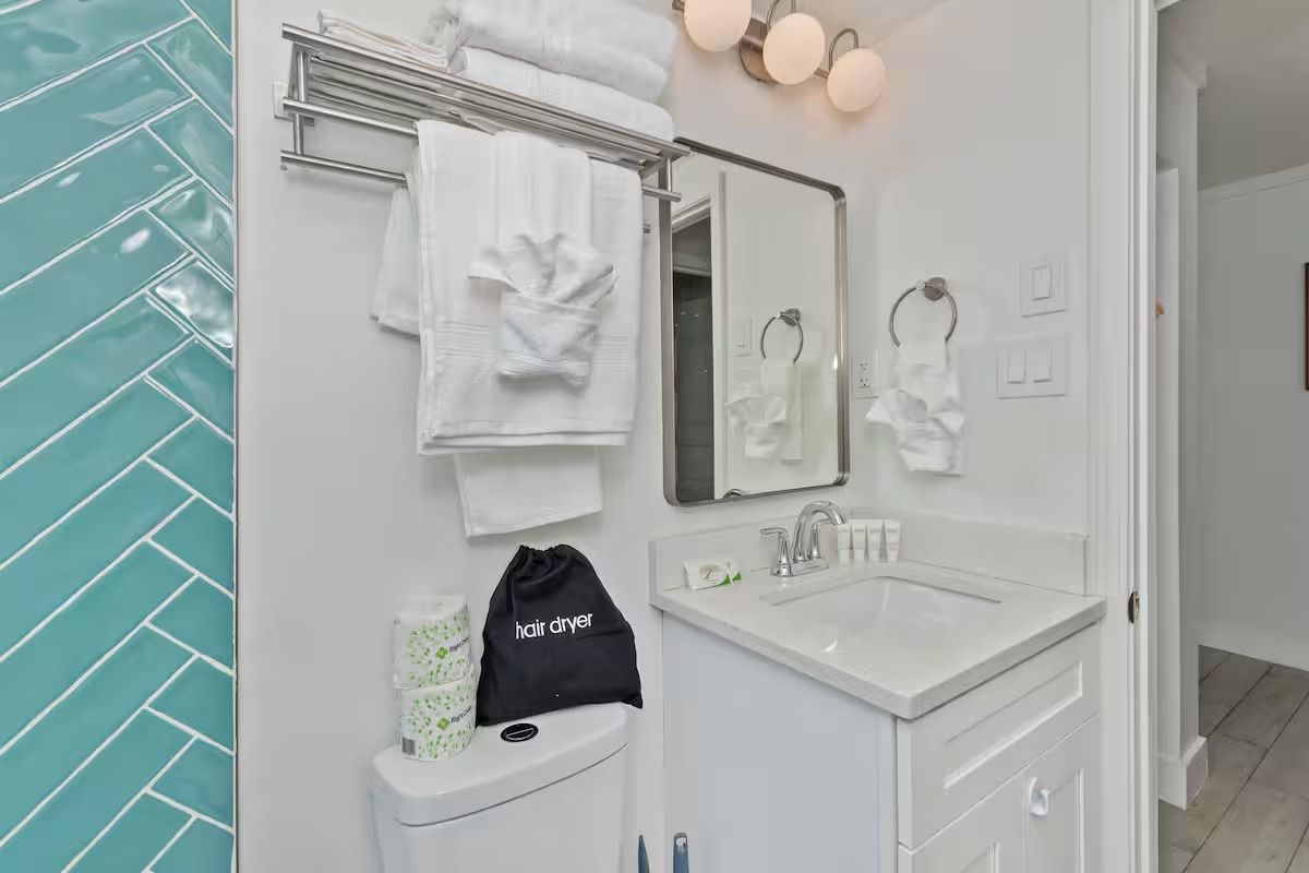 Bathroom with white vanity, towels, and turquoise tiled shower.