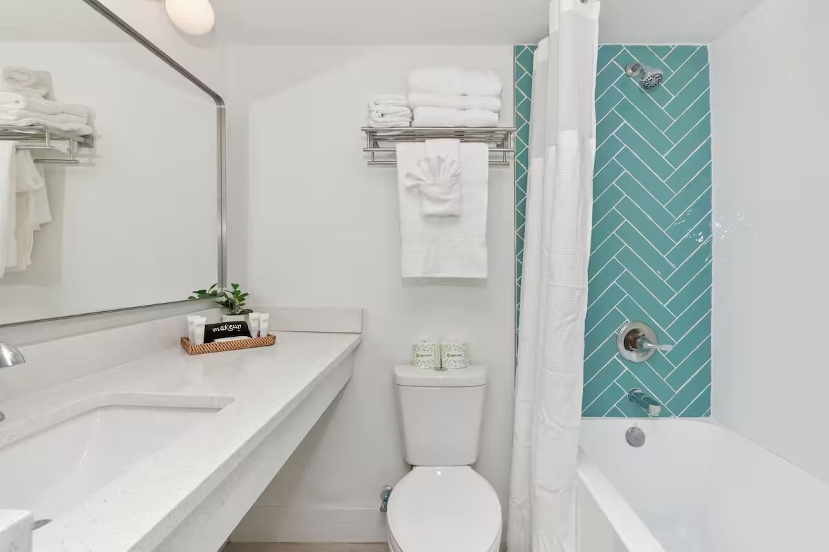 A bright white bathroom with a turquoise herringbone tile shower and a white vanity.