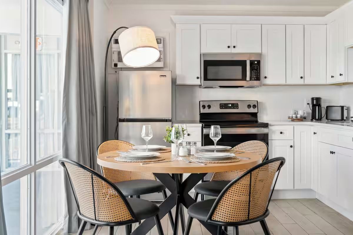 A bright kitchen with a round wooden table set for four, surrounded by woven chairs.