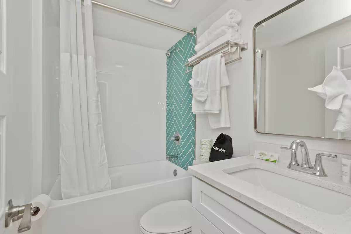 Bathroom with white fixtures, teal accent tile, and folded white towels.