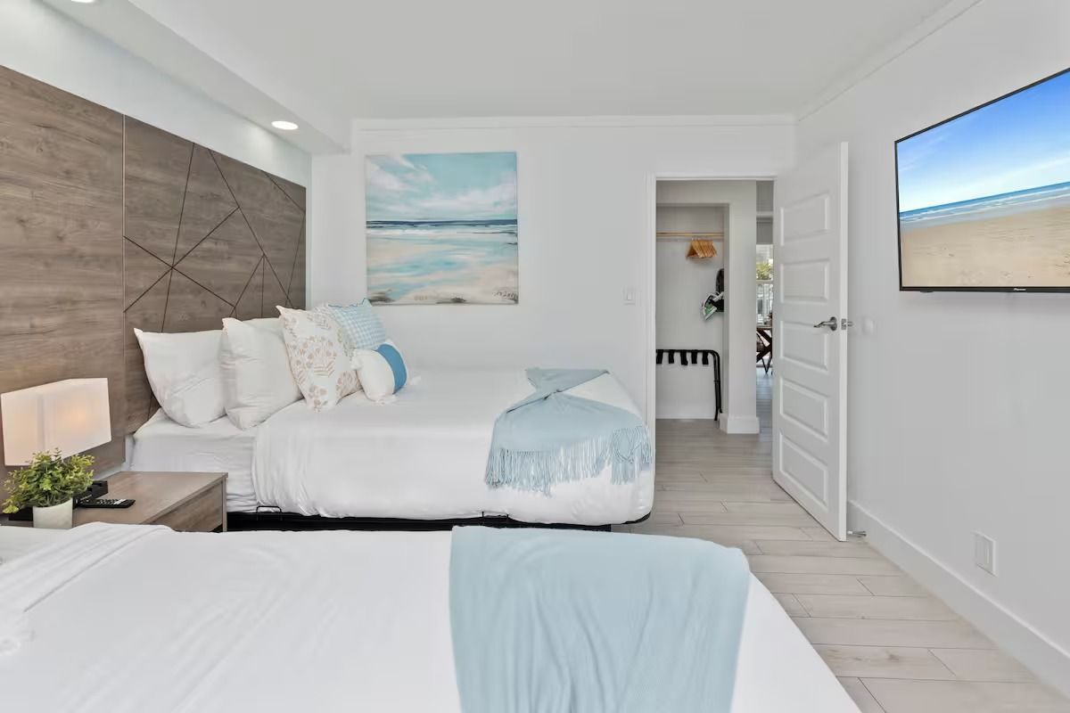 Bright bedroom with two beds, a TV, and a door leading to a closet. Blue and white decor.