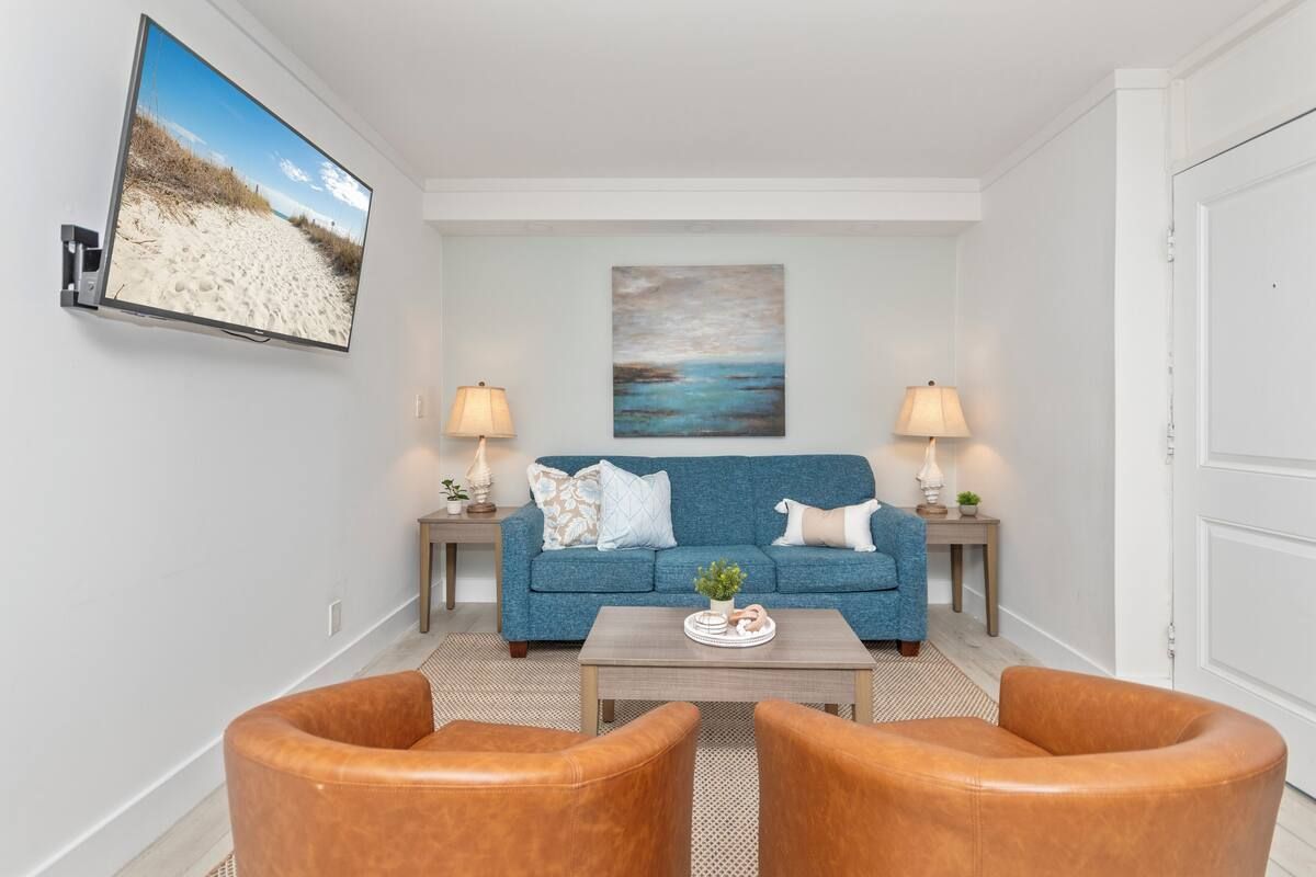 Living room with blue sofa, two brown armchairs, TV, and artwork.