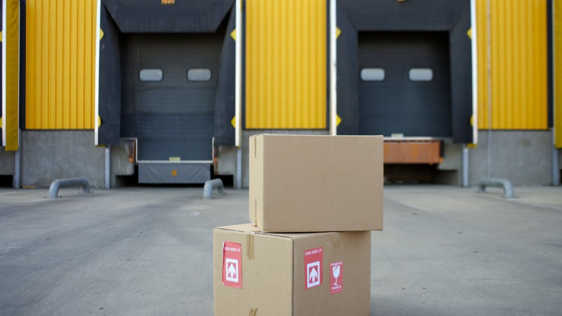 Cajas de cartón apiladas frente a muelles de carga con puertas superiores amarillas.