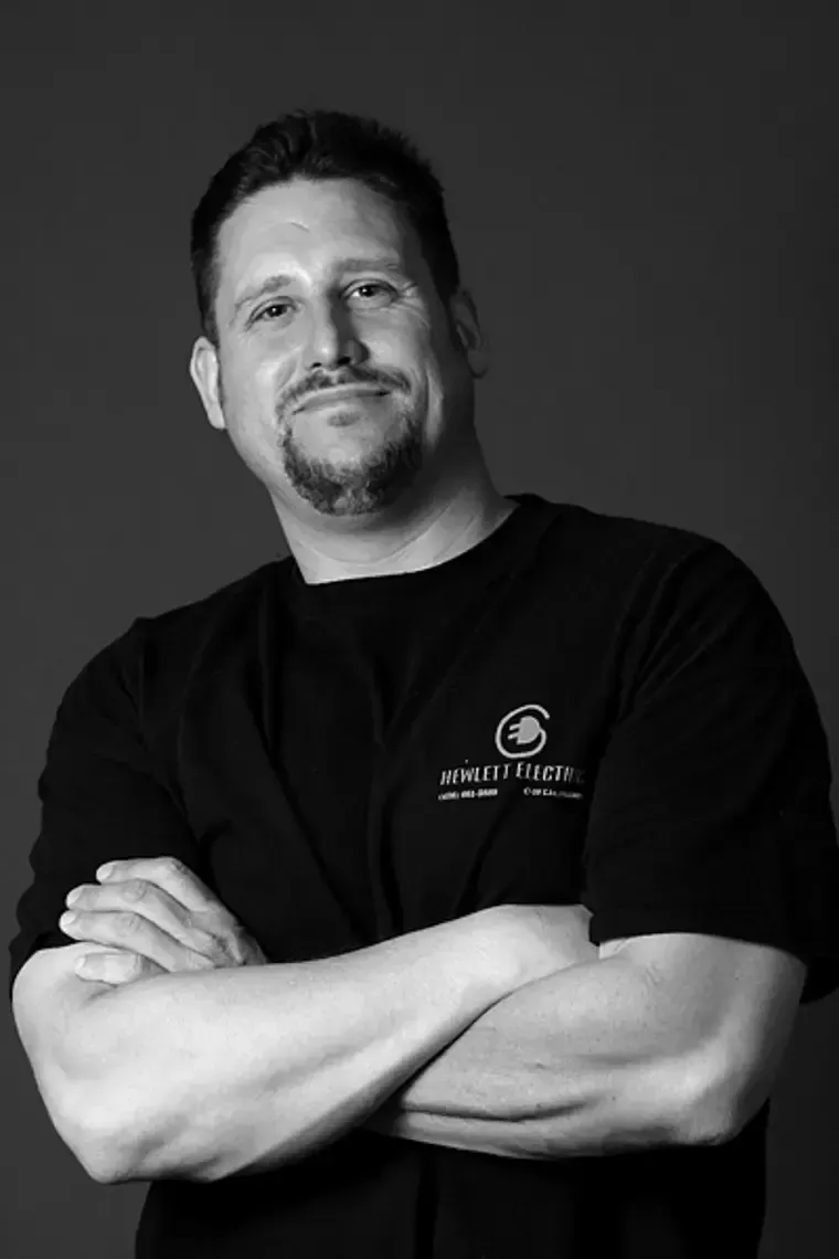 A man with his arms crossed is wearing a black shirt that says specifications