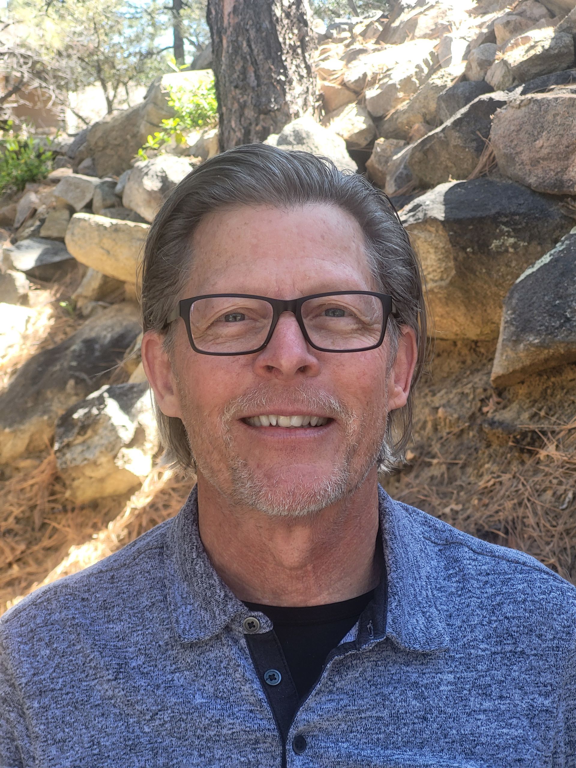 Woman with curly red hair, smiling, wearing a dark sweatshirt with the word “Gold” on the sleeve, outdoors.