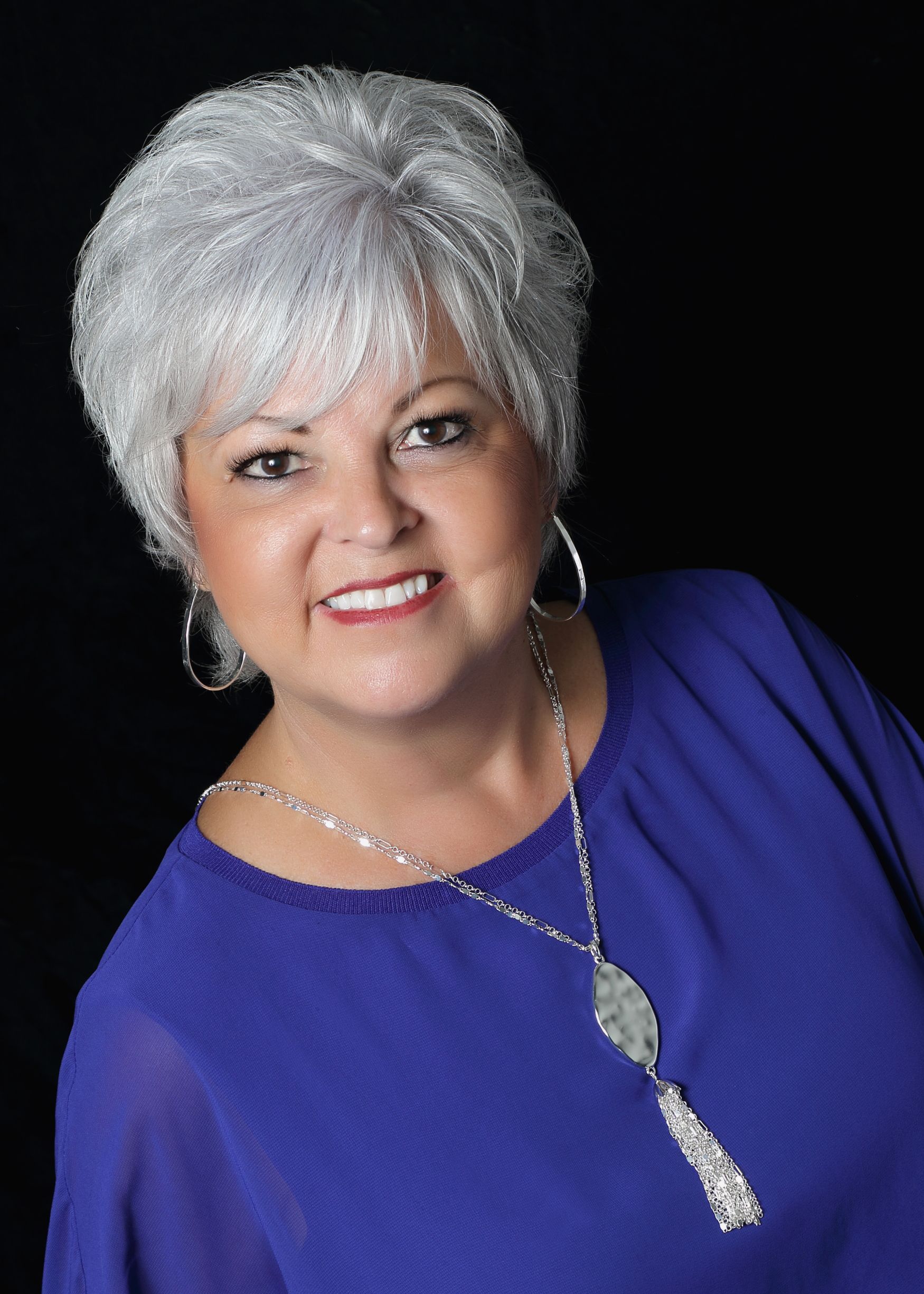 A woman with white hair is wearing a blue shirt and a necklace.