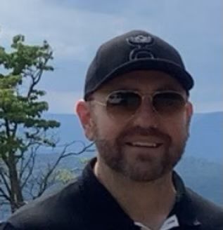 A man with a beard is wearing a hat and sunglasses.