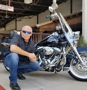 A man is kneeling in front of a harley davidson motorcycle
