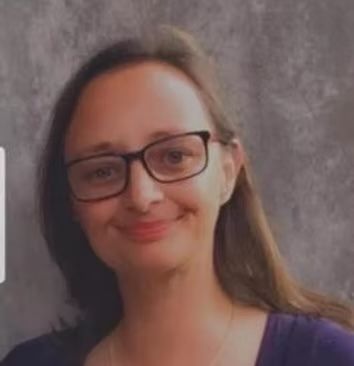 A woman wearing glasses and a purple shirt is smiling.