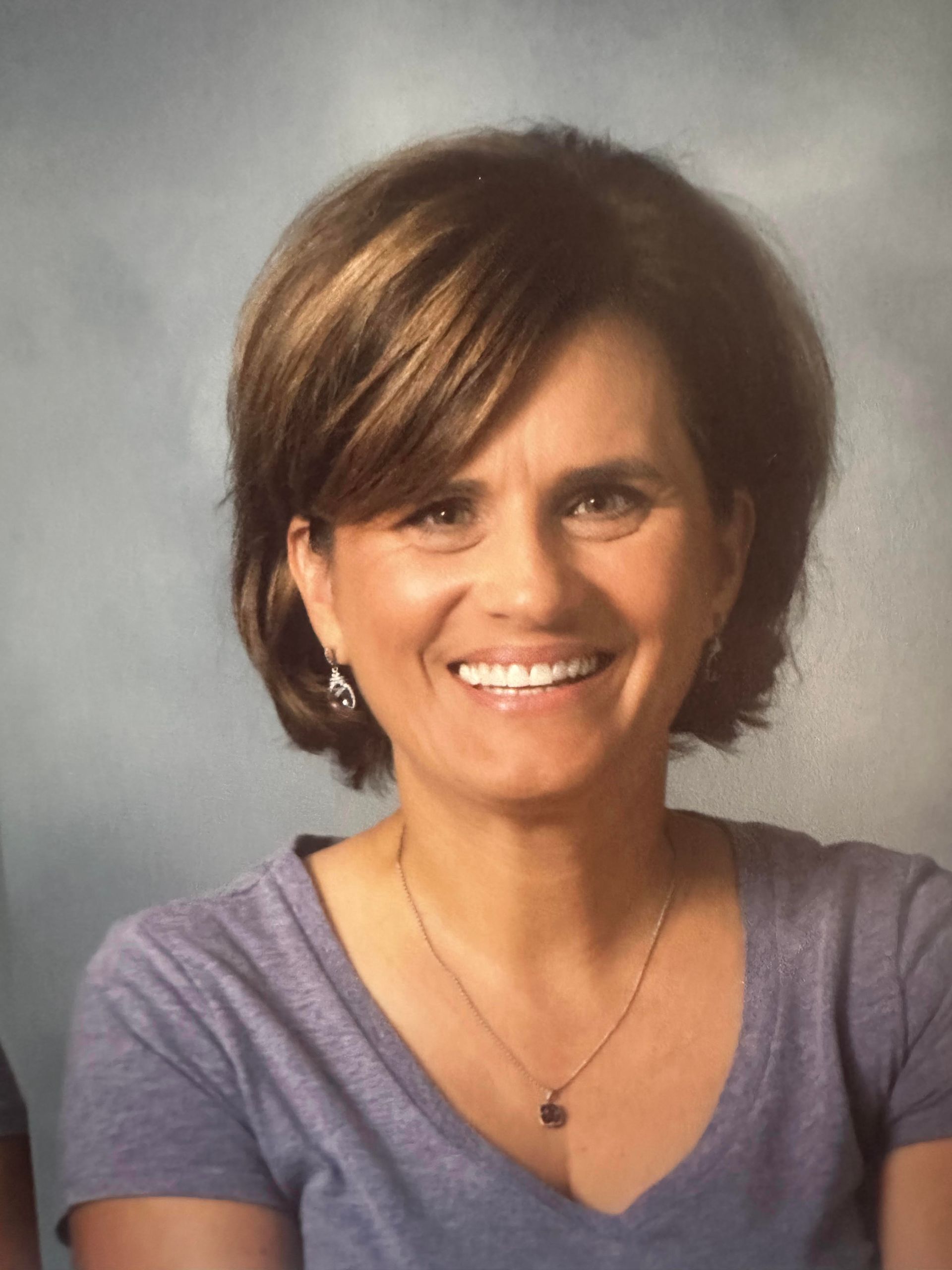A woman wearing a purple shirt and a necklace is smiling for the camera.