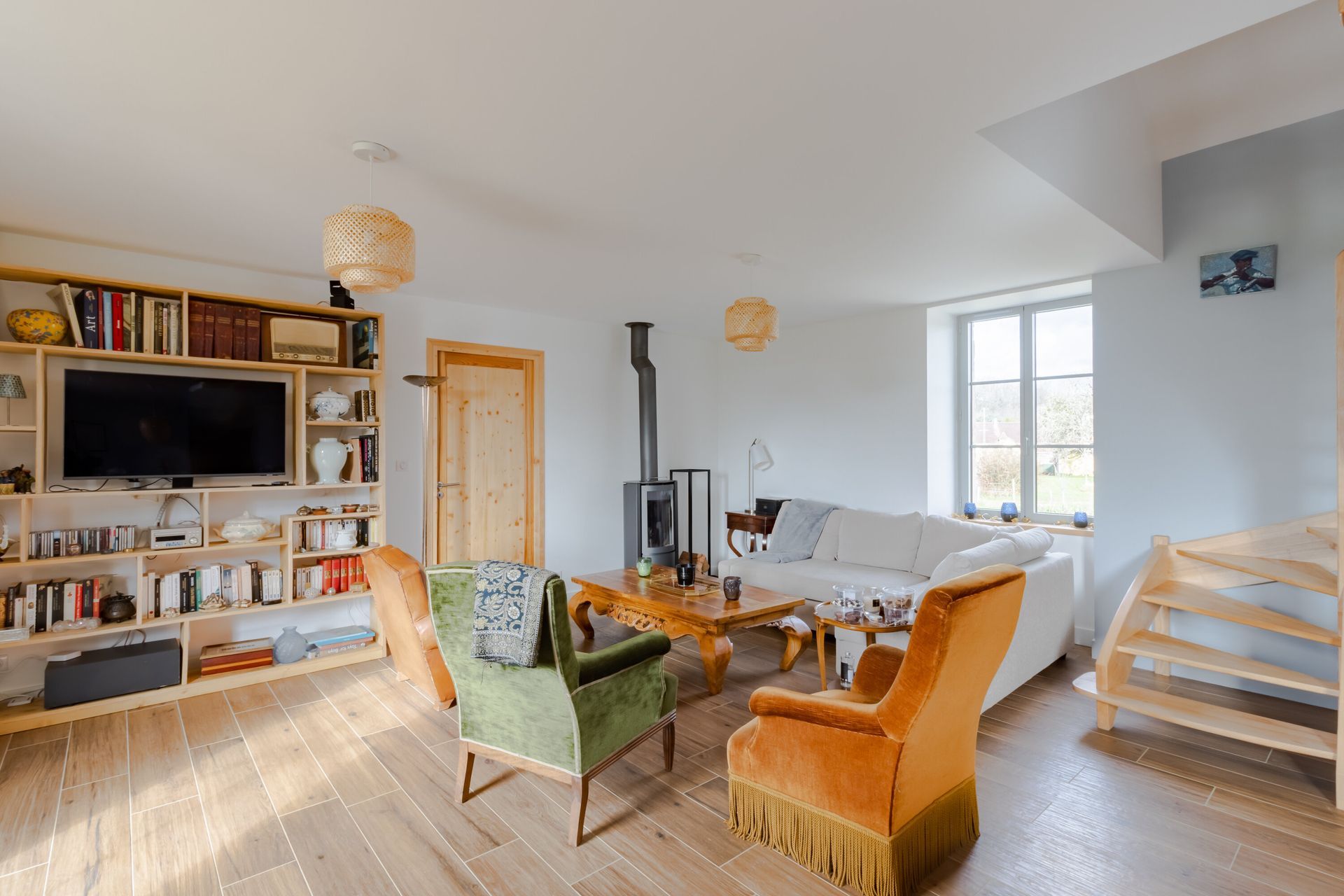 Salon chaleureux avec parquet, cheminée, étagères et fauteuils colorés.