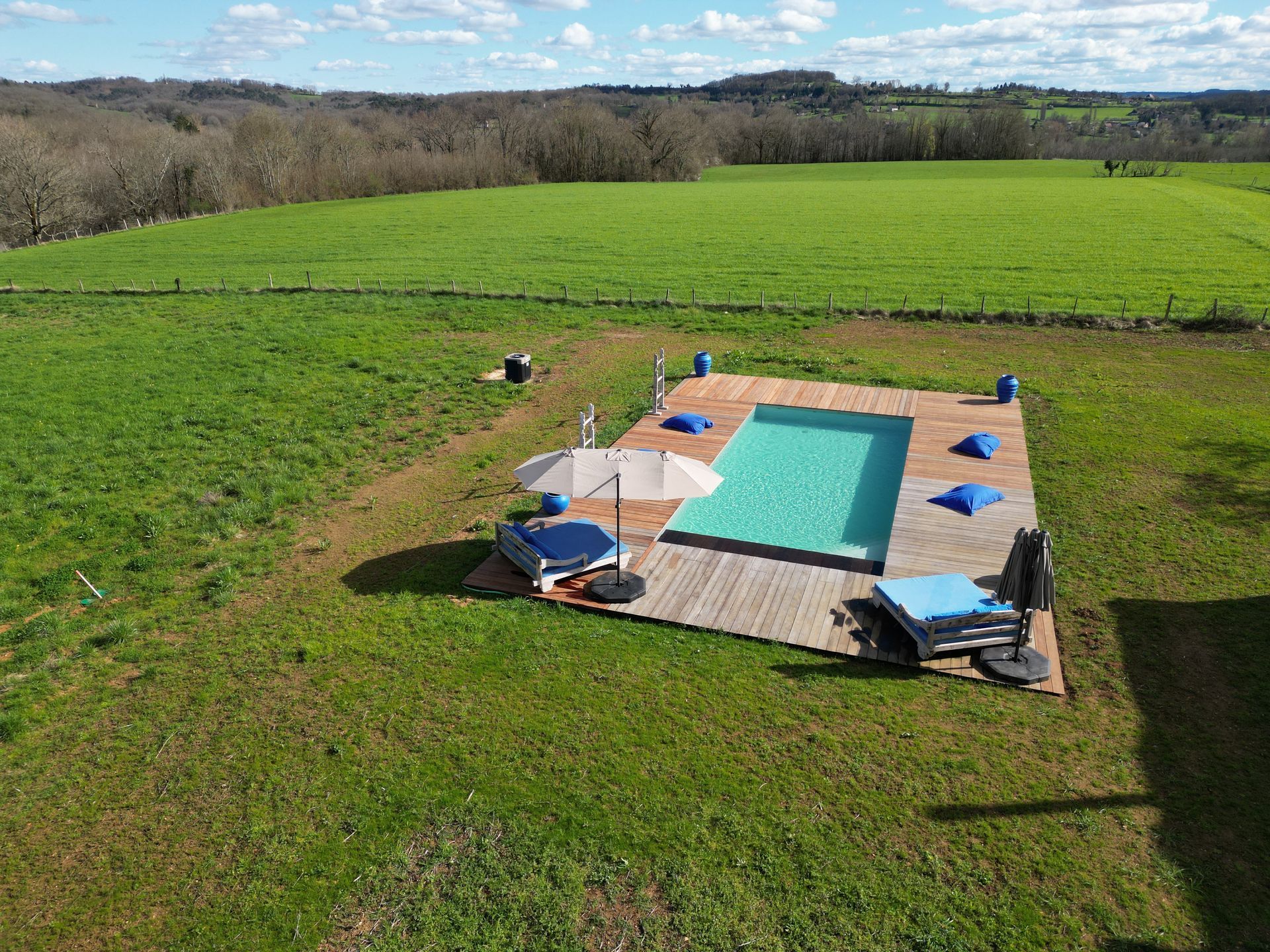 Piscine dans un terrain herbeux avec terrasse en bois, chaises longues et parasol.