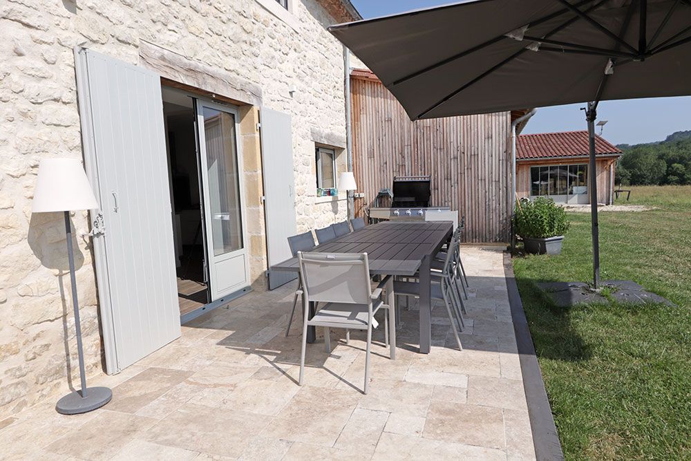 Patio avec table et chaises à l'extérieur d'une maison en pierre avec parasol et pelouse.