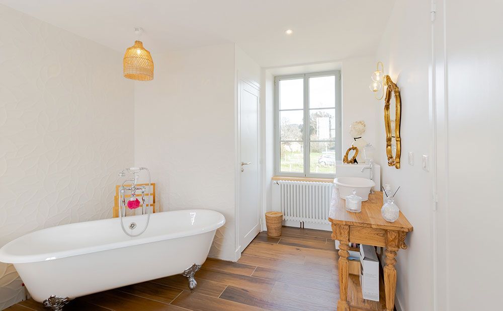 Salle de bain blanche avec baignoire sur pieds, vanité en bois et fenêtre.