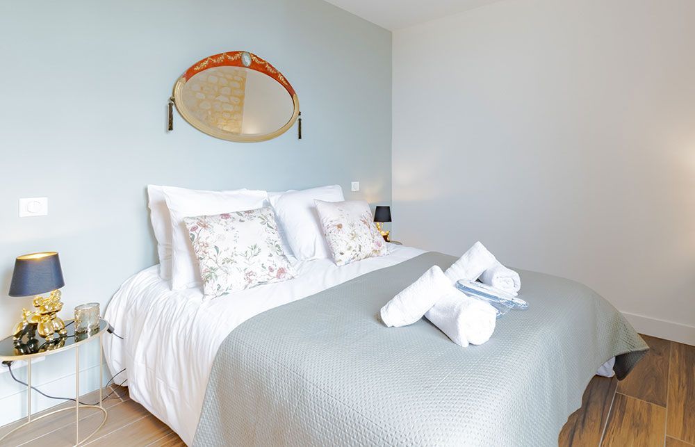 Chambre avec un lit double, oreillers, serviettes, table de chevet, lampe et miroir mural décoratif.