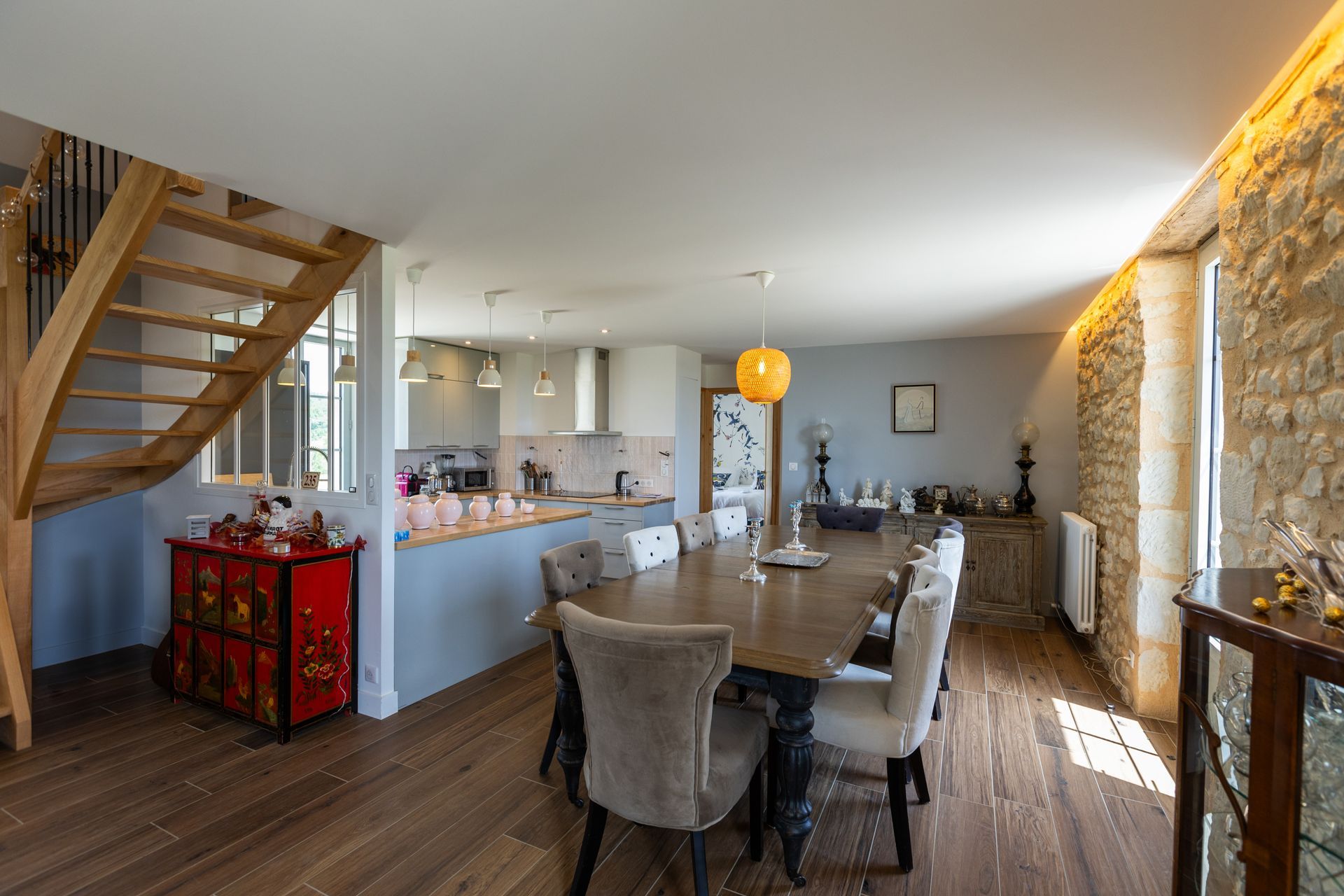 Une salle à manger et une cuisine ouvertes avec une longue table en bois, un mur en pierre et un escalier en bois.