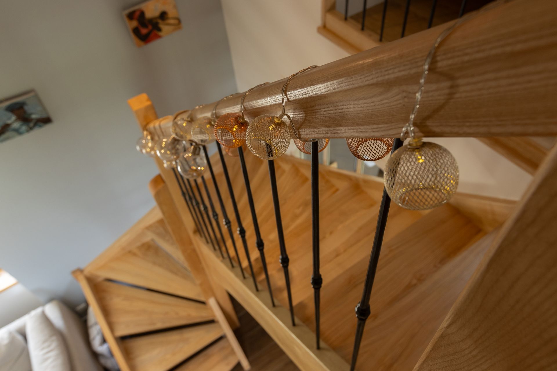 Escalier en bois avec rampe en métal, décoré de guirlandes lumineuses rondes, dorées et suspendues.