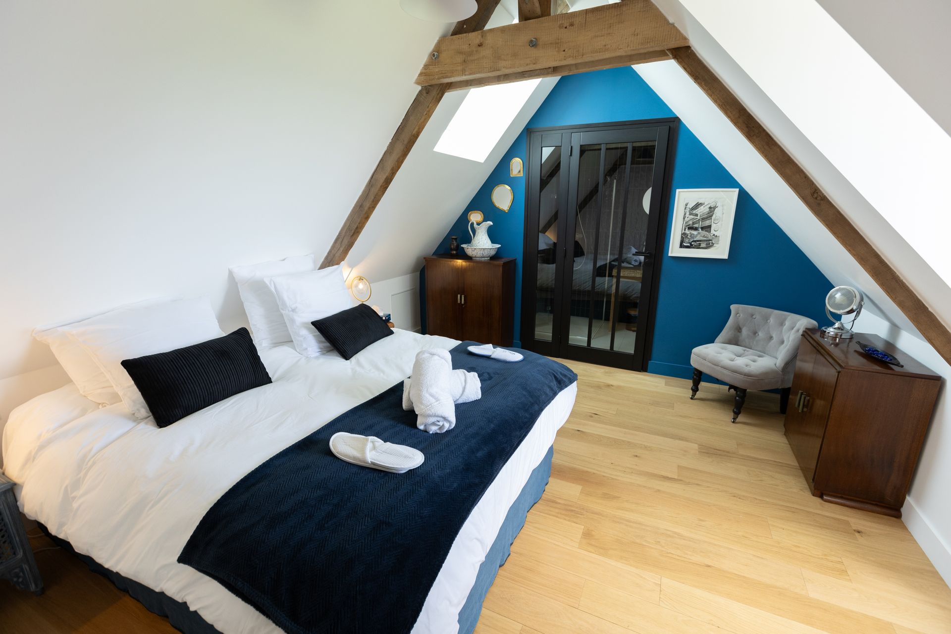 Chambre mansardée confortable avec un lit, un mur bleu, des poutres en bois et une porte sombre.