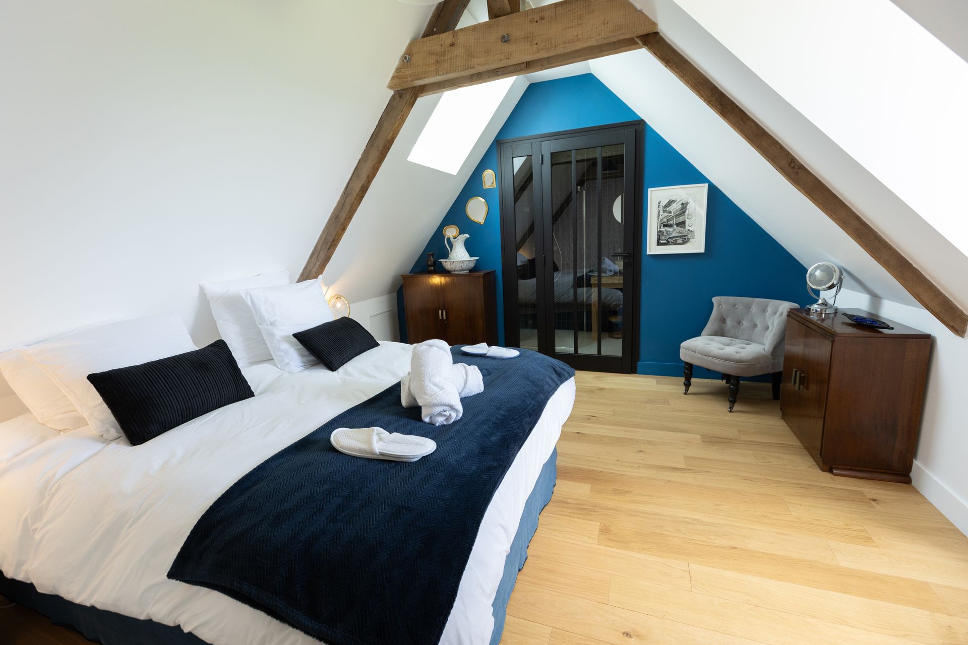 Chambre avec un lit, une chaise et un mur bleu foncé. La pièce est dotée de parquet et d'un plafond mansardé.