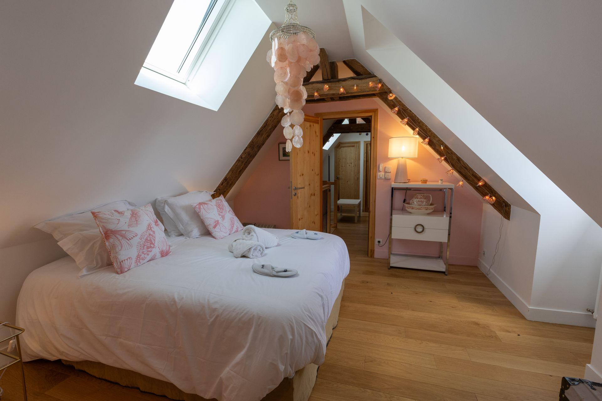 Chambre dans un grenier de cottage avec un lit double, des murs roses et une petite porte menant à une salle de bain.