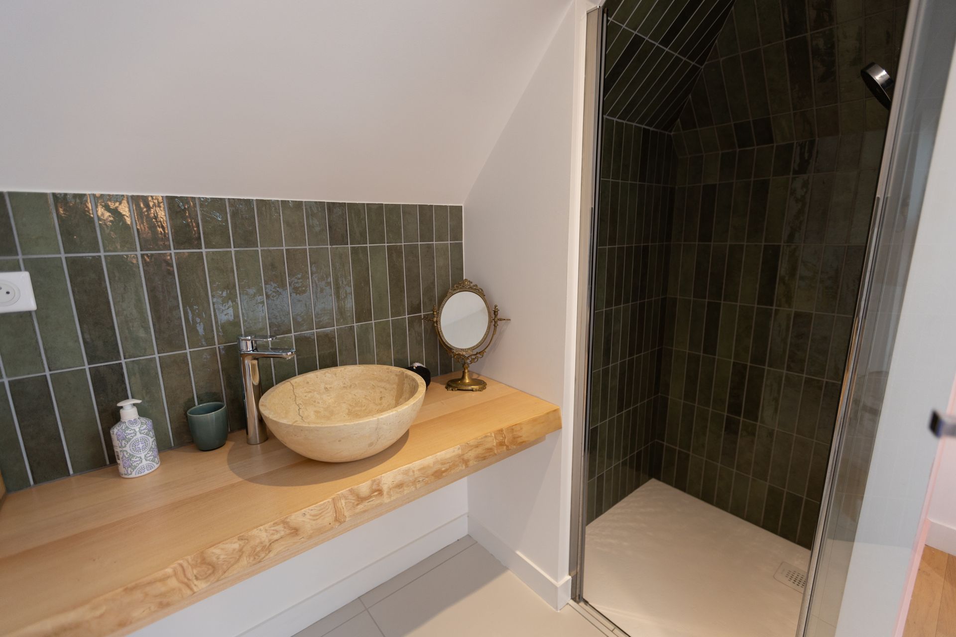 Salle de bain avec comptoir en bois, lavabo en pierre, mur carrelé vert et douche.
