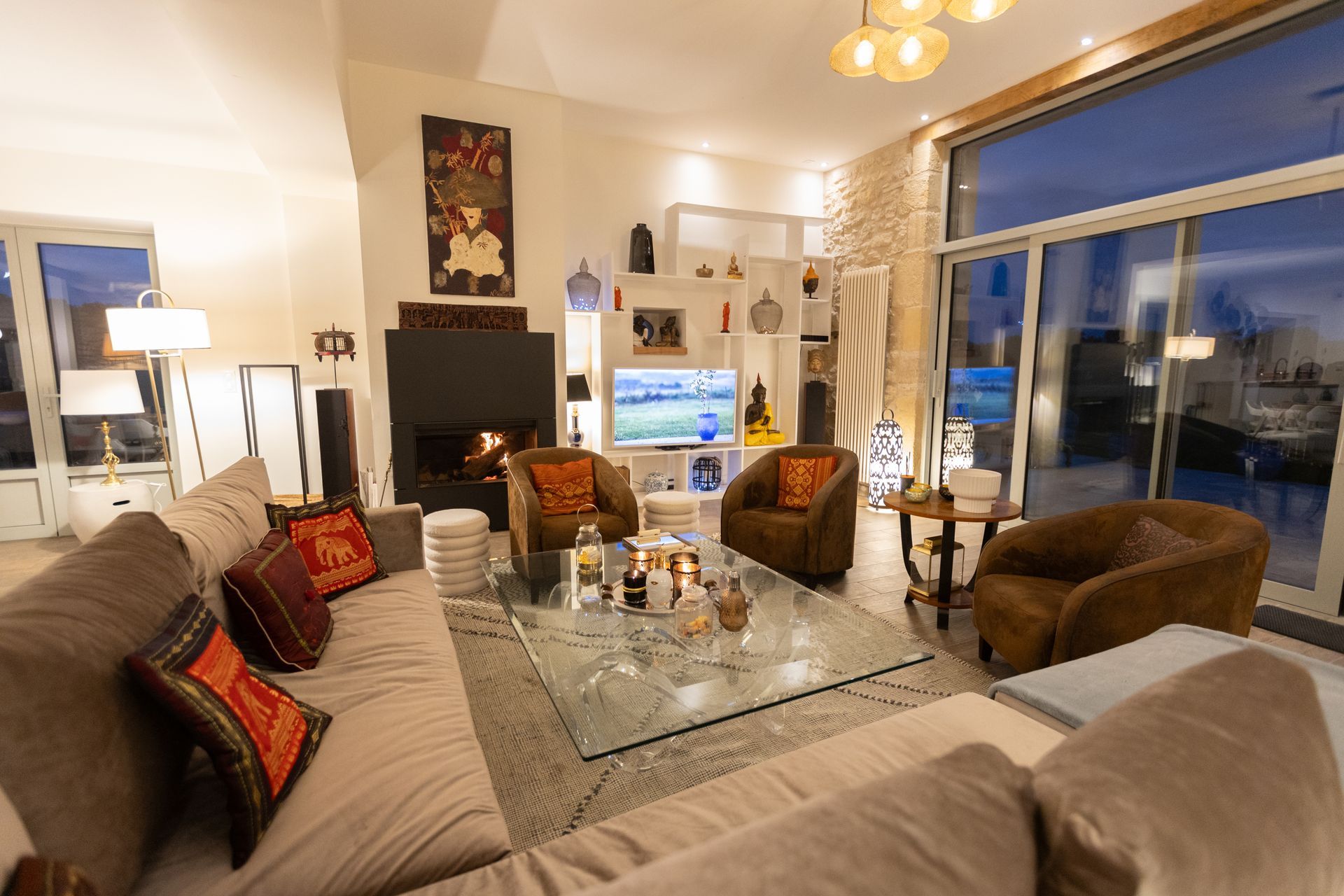 Salon chaleureux avec un grand canapé, deux fauteuils, une cheminée et une grande fenêtre avec vue sur l'extérieur.